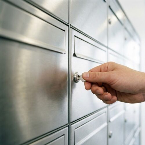 A close-up of a hand holding a silver key near modern metal mailboxes.